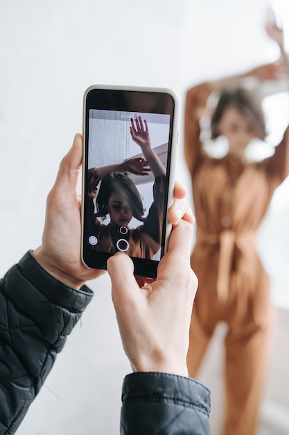 Male hands taking photo of a model with smartphone. Selective focus on screen with sensual brunette. Real one is blurred.