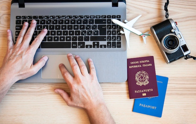 Male hands typing on modern laptop for booking an airplane flight Man plans couple tour with passports on the desk for holiday Different nationality passports Booking couple holiday concept