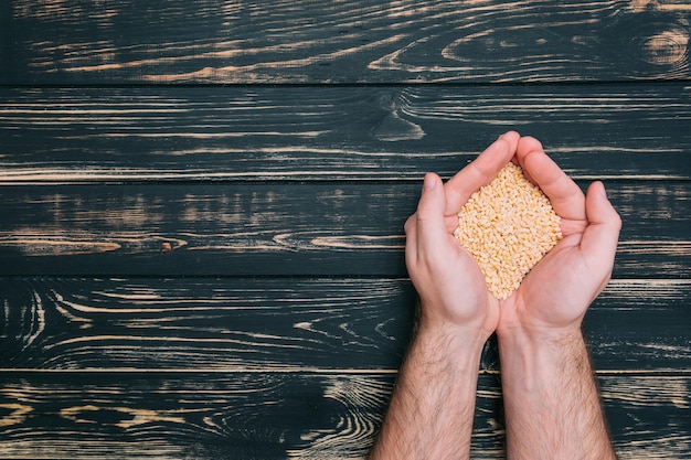 In male hands wheat grain on black wooden background