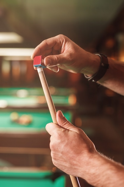 The male hands wipes a cue with chalk.