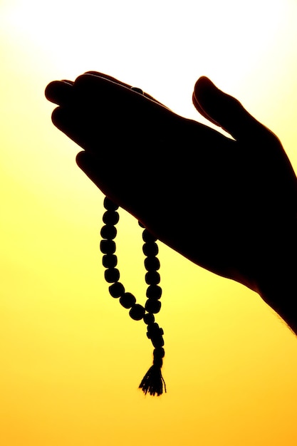 Male hands with rosary on yellow background