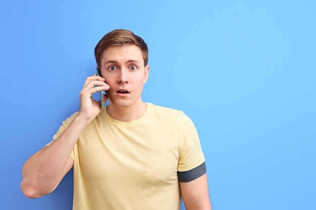 Male having conversation on phone, talking with someone and sharing news, stand in shock while listening to talk. isolated blue background