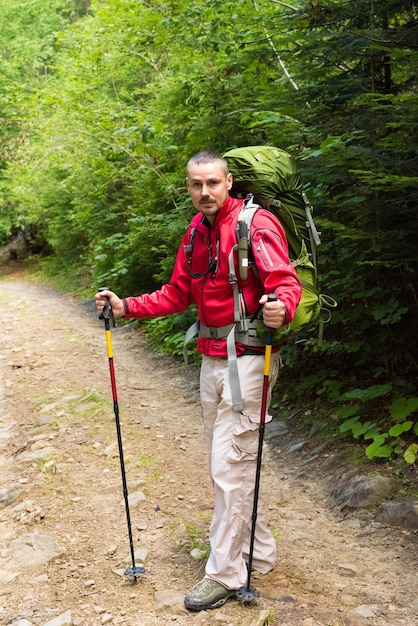 Male hiker with big green traveling rucksack and trekking pole moving up on the mountain trail