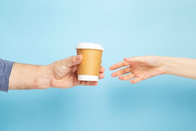 Male holds hand paper cup with coffee female takes cup on blue background