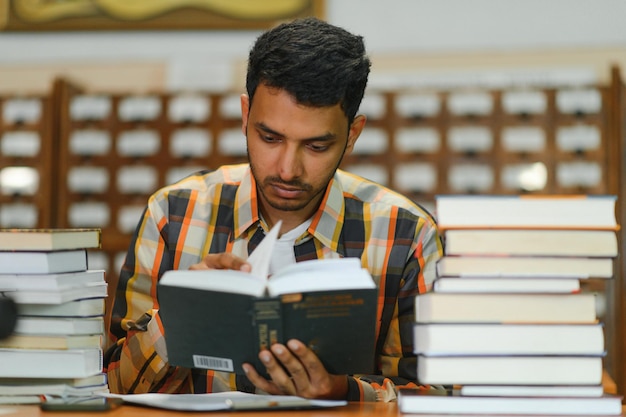 Male indian student at the library with book