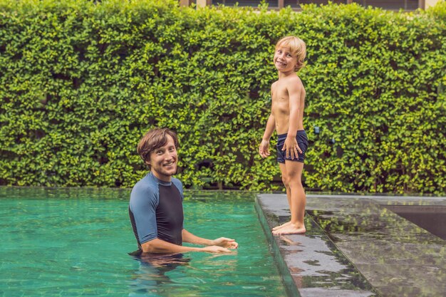 Male instructor swimming for children teaches a happy boy to swim in the pool.