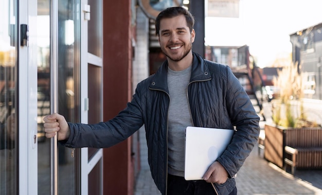 A male it specialist with a laptop in his hands enters the office building with a wide smile on his