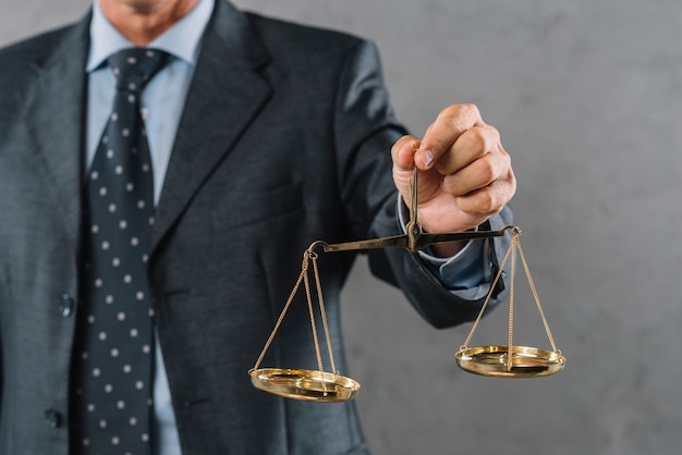 Male lawyer's hand showing justice scale against gray textured background