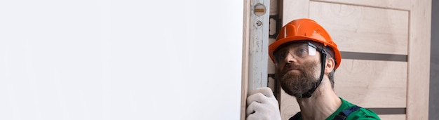 A male locksmith installs a door in an apartment The guy checks the accuracy of measurements with a building level