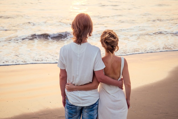 Male making proposal with engagement ring to his girlfriend at sea beach.St.Valentines Day concept.beautiful woman in white dress and man enjoying the sunset on the sea