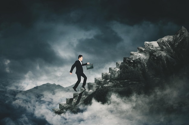 Male manager climbing stairs toward mountain peak