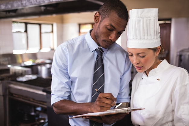 Male manager and female chef writing on clipboard in kitchen