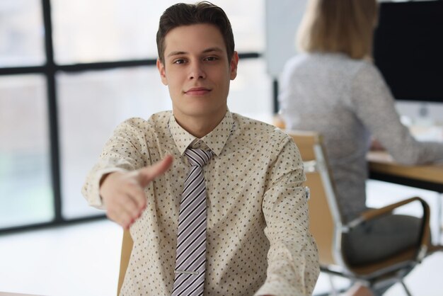 Male manager offers his hand for handshake while sitting at office desk concept of recruitment