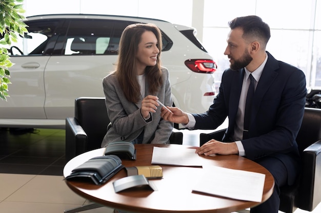 Male manager selling a new car to a young woman in a car dealership car rental concept