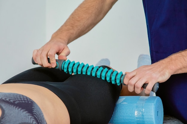 A male masseur conducts spa treatments using a special massage roller for a young woman who is lying