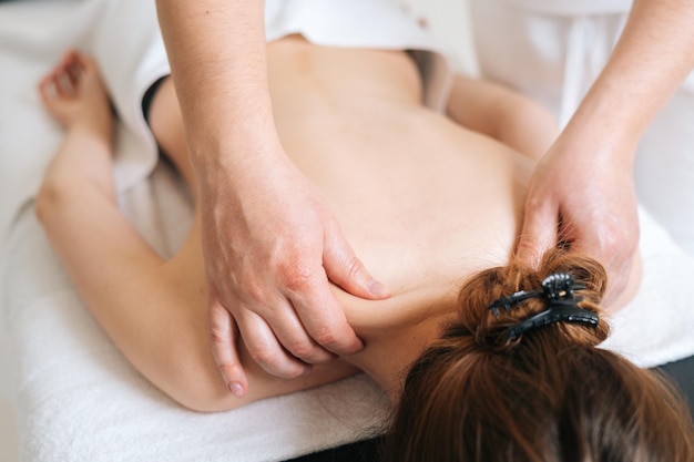 Male masseur with strong hands professionally massaging scapulas and shoulders to female client