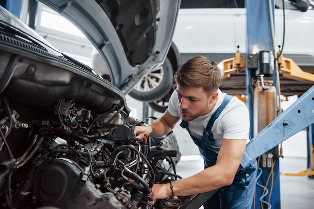 Male mechanic on the job. Employee in the blue colored uniform works in the automobile salon