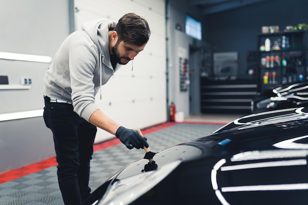 Photo male mechanic using car detailing brush kit on his clients black sports car professional maintenance