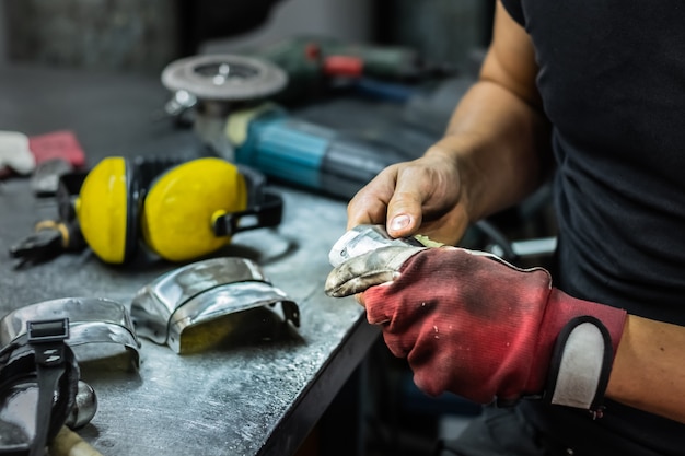 Photo male metal worker assembling piece of medieval armour suit. man hands treating metal parts of hardware in a workshop