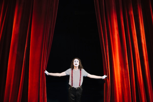 Male mime artist performing on stage near red curtain