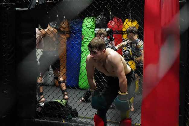 Male mma fightter resting in the cage after boxing rounds at the gym