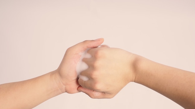 Male model is interlock fingers and rub mid-joints with foaming hand soap on white background.