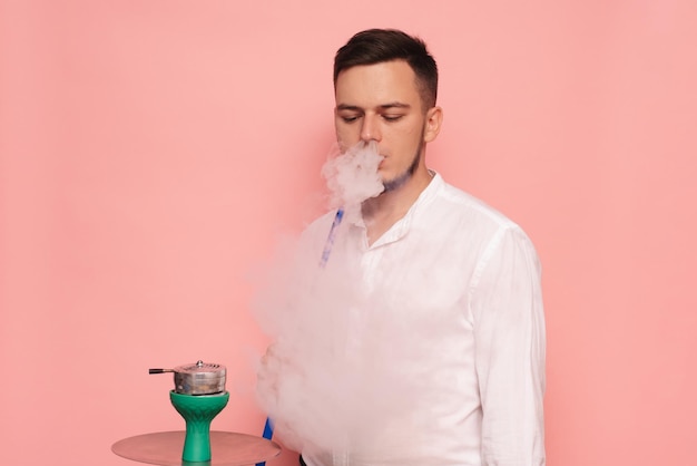 A male model smokes a hookah sheesha and enjoys it Pink background