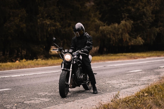 male motorcyclist in protective uniform and helmet with custom motorcycle cafe racer in autumn on th