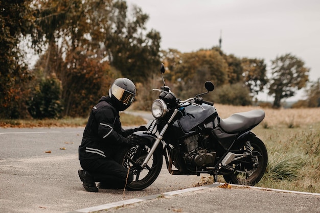 male motorcyclist in a warm jacket and helmet in cold autumn weather on the road with a motorcycle c