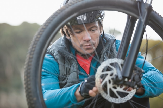 Male mountain biker examining front wheel of his bicycle