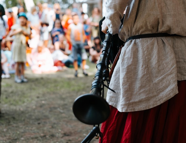 A male musician in a medieval costume holding an old traditional bagpipe instrument Folk concert outdoors Closeup rear view