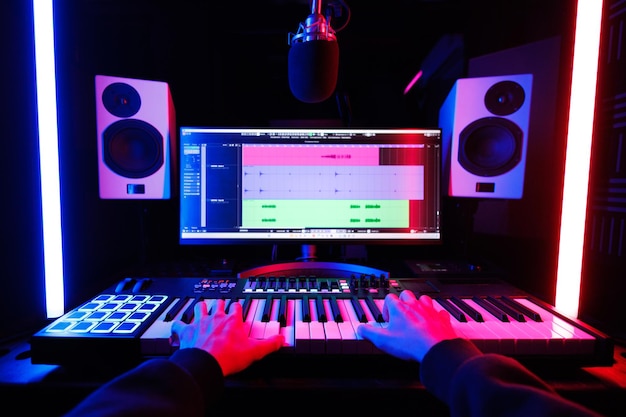 A male musician playing a midi keyboard synthesizer in a recording studio focused on his hands