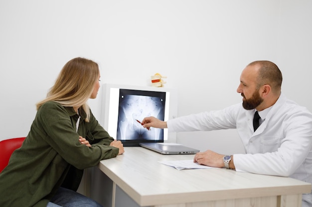 Male orthopedist doctor showing xray to female patient at medical office