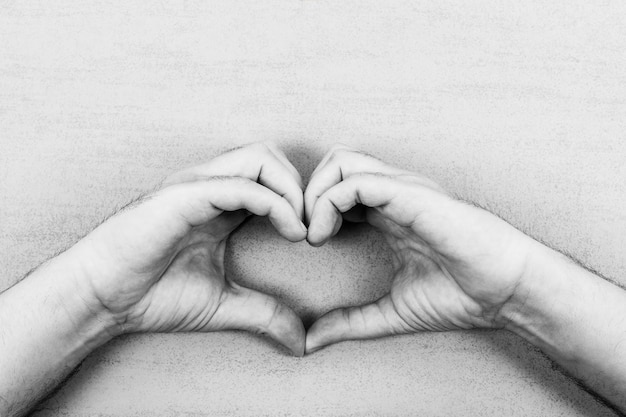 Male palms with a heart of fingers on a gray background black and white photo