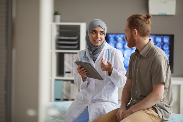 Male patient listening to his doctor while she telling about the disease using digital tablet they sitting on couch at hospital