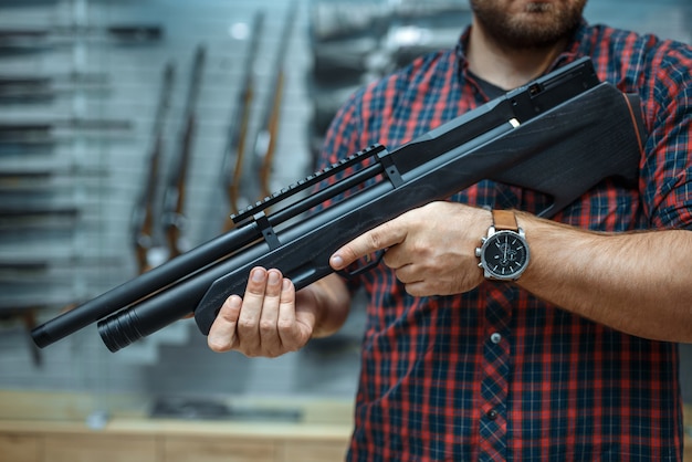 Male person with pneumatic rifle at showcase in gun shop