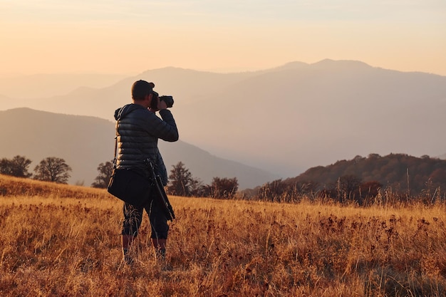 Male photographer standing and working at majestic landscape of autumn trees and mountains by the horizon