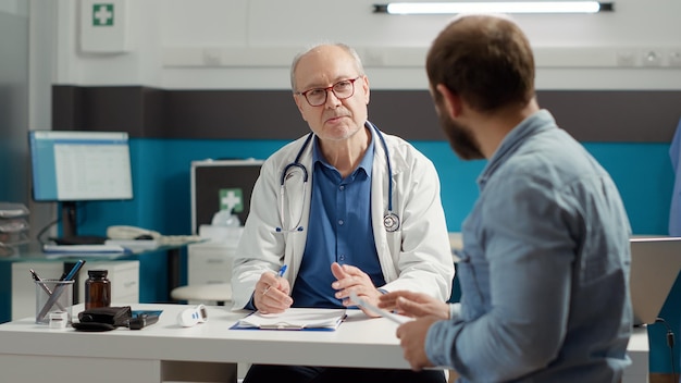 Male physician writing checkup visit report on medical files, preparing prescription medicine to help with health care system. Treatment at consultation appointment to cure disease.