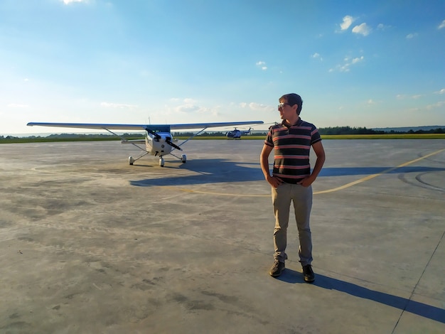 Male pilot in glasses standing near a small plane on the airfield