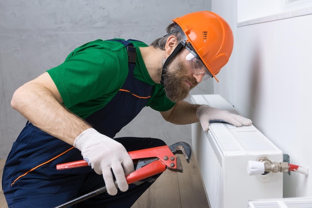 A male plumber installs a radiator in the heating system of an apartment