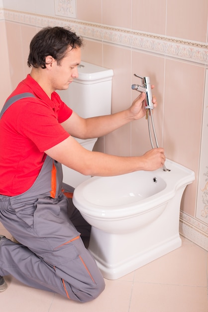 Male plumber repairing toilet in the apartment.