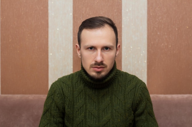 Male portrait a man in a green sweater sitting on a sofa