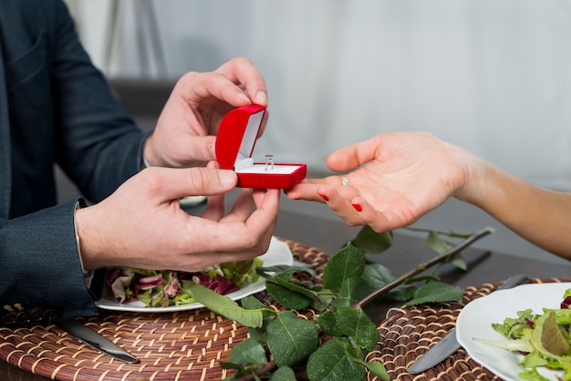 Photo male presenting gift box with ring to female at table with dishes and bloom