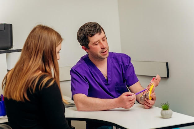 Male Proctologist doctor showing artificial model of human rectum to patient in hospital during consultation