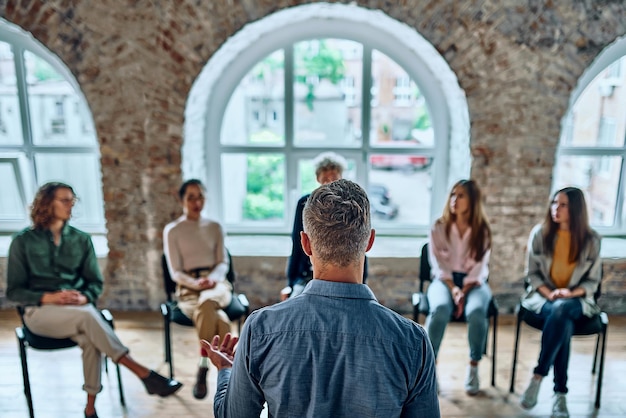 Male psychotherapist talking with her group during session Back view Selective focus