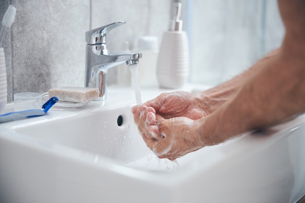  male rinsing the soap off his hands in the bathroom