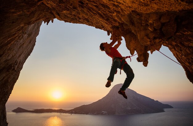 Male rock climber on challenging route on cliff in cave at sunset