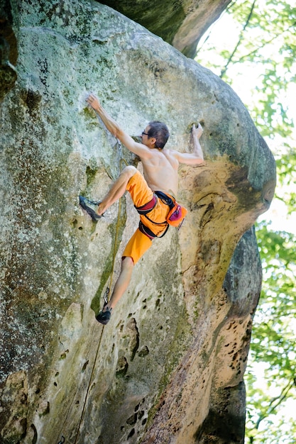 Male rock climber climbing with rope on a rocky wall