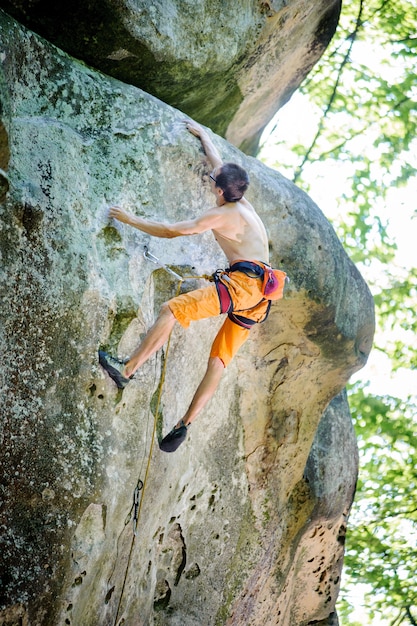 Male rock climber climbing with rope on a rocky wall