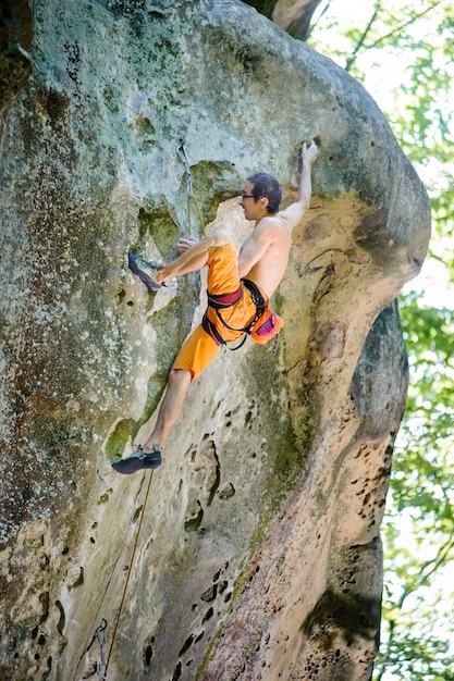 Male rock climber climbing with rope on a rocky wall